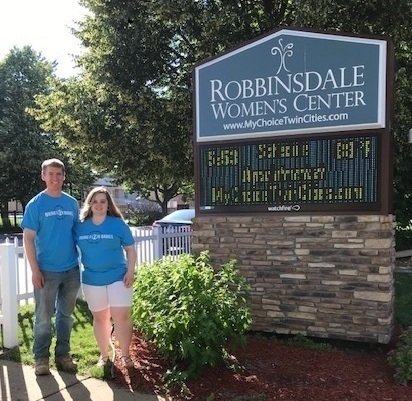smiling couple facing camera and standing near Robbinsdale Women's Center sign